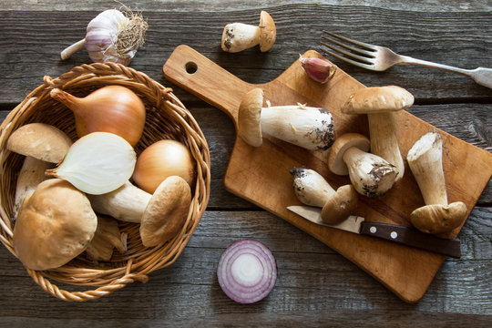 Fresh white mushrooms in basket and ingredients for mushroom's cream-soup on a rustic wooden board, overhead view.