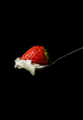Whipped cream and a strawberry in a silver spoon on black backgr