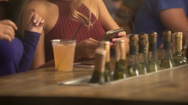 Glamorous blonde ladies watching video on smartphone, having fun at party in bar