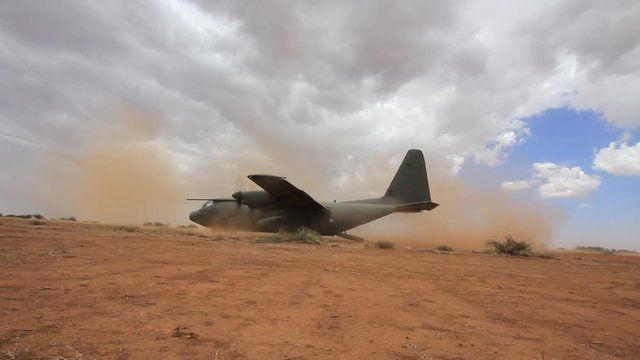 Aircraft lands on field airstrip during training exercise with British Army. Soldiers of Parachute Regiment practice deploying field gun.
