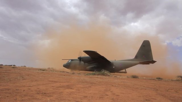 Aircraft lands on field airstrip during training exercise with British Army. Soldiers of Parachute Regiment practice deploying field gun.