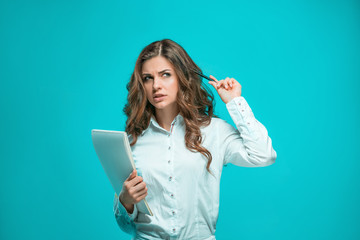 The thoughtful young business woman with pen and tablet for notes on blue background