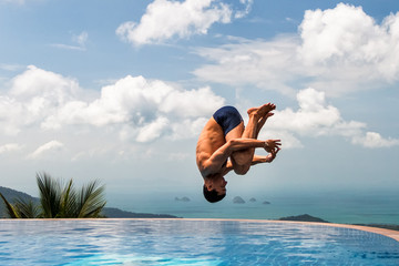 Young athletic man jumps into the pool at the top of the mountain
