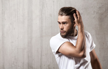 Handsome bearded man in a blank white t-shirt with stylish hair on a cement wall