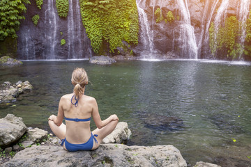 Girl practicing yoga and meditating in lotus position in nature