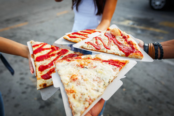 A group of people on street taking slices of pizza 