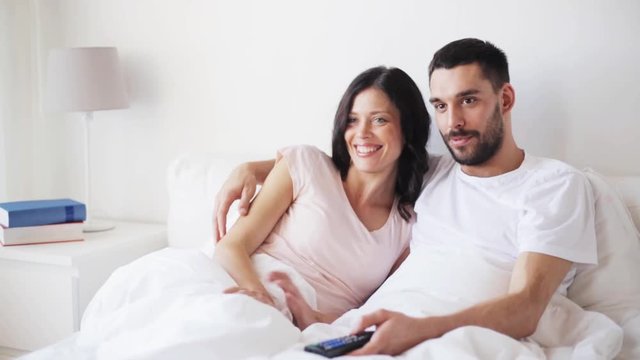 happy couple watching tv in bed at home