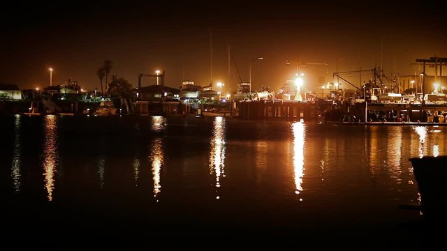 A wide angle stationary shot of an industrial fishing dock at night.