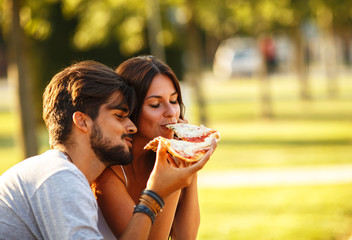 Young couple  sitting on park bench and eating pizza.Fast food.