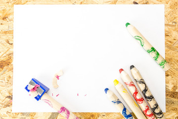 Bunch of thick colorful pencils for children and sharpener with shavings, on blank sheet of paper,...