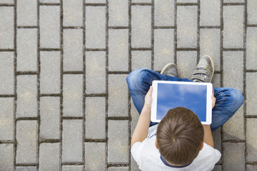 Fototapeta premium Child with tablet computer sitting outdoors. Education, learning, technology, friends, school concept. Top view.