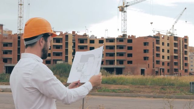 Engineer with blueprint at construction site. Master builder in hard hat. HD.
