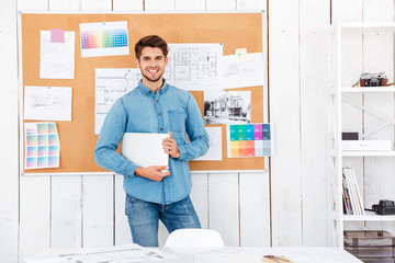 Cheerful man standing at the task board and holding laptop