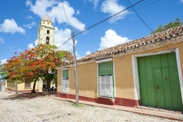 Fototapeta na wymiar Scenic view of traditional colonial architecture with a tropical flame tree and the bell tower of the church of San Francisco de Asis in Trinidad, Cuba