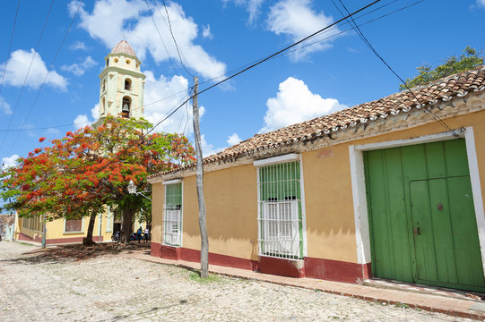 Scenic view of traditional colonial architecture with a tropical flame tree and the bell tower of the church of San Francisco de Asis in Trinidad, Cuba