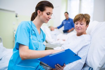 Nurse showing clipboard to patient in hospital ward