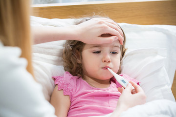 Mother measuring temperature of her ill kid. Sick child with high fever laying in bed and mother...