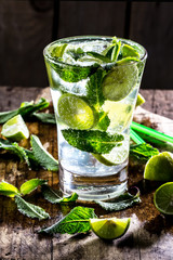 Glass of alcohol cocktail or lemonade. Mohito cocktail with lemon, lime, mint, ise cubes. Cold drink. Fresh lime and mint on wooden background