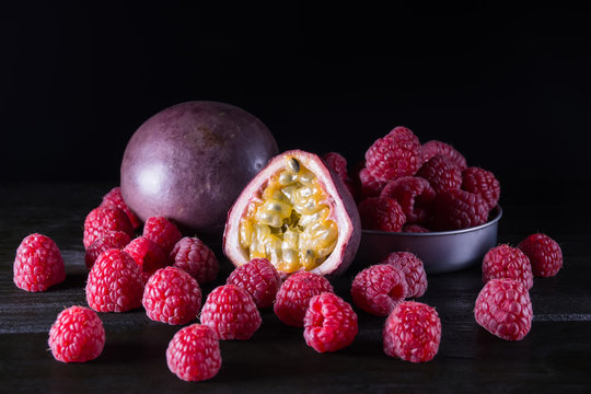 Passionfruit and raspberry on black wooden table on dark backgro