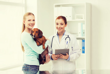 happy woman with dog and doctor at vet clinic