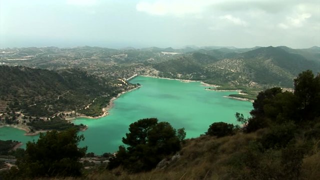 Wide shoot from above of water reservoir "Embalse de Amadorio" with small trees in front  in Orxeta, Spain. Shoot from nearby mountain.