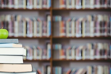 stack of books and green apple with library background