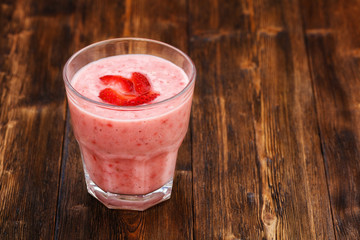 Strawberry milk smoothie in a glass, wooden background