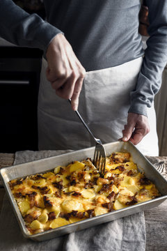 Cutting tartiflette in the baking tray  on the wooden table  vertical