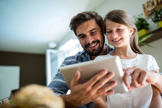 Father and daughter using digital tablet in the living room