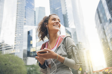 Young woman runner wearing armband and listening to music on ear