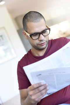 Portrait of hispanic guy with eyeglasses reading newspaper