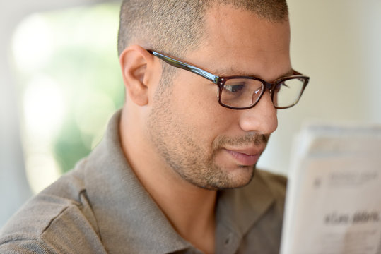 Portrait of hispanic guy with eyeglasses reading newspaper