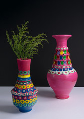 Still life of two artistic painted colorful handcrafted pottery vases, and green plant branches with harsh shadow on white table and black wall