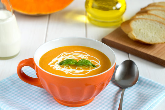 Squash soup with cream in a bowl on the wooden table.