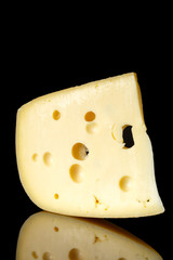 a piece of Swiss cheese with large holes on a black background with reflection. minimalist style of food art. cheese closeup