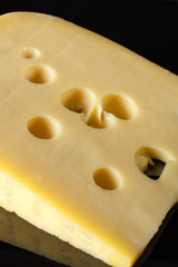 a piece of Swiss cheese with large holes on a black background with reflection. Food art in low key. Yellow on black