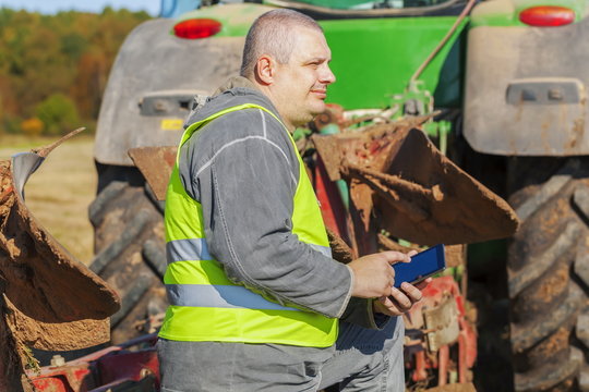 Farmer with tablet PC near tractor on field