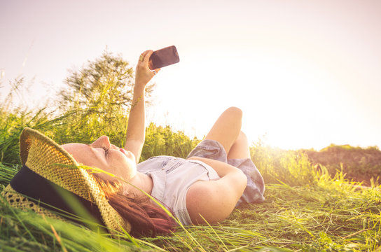 Young happy girl taking a selfie lying on the grass. 