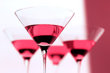 Four Cosmopolitan martini glass cocktails from low angle with bright pink background