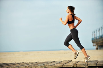 Attractive fit young woman running on Santa Monica Beach boardwalk pacific ocean and pier in...