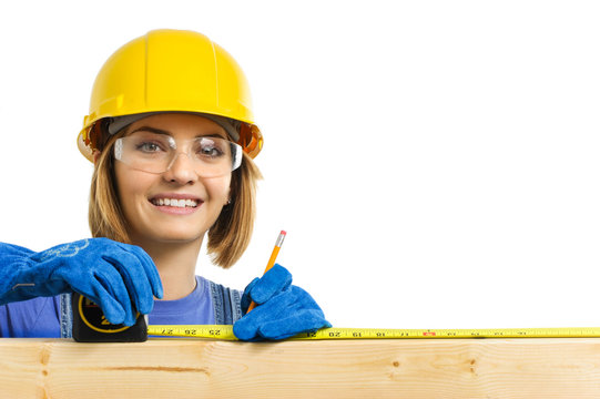 Cute Young Woman In Hard Hat And Safety Glasses Uusing Tape Measure On Board Isolated On White Background