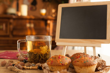 Chinese flower jasmine tea with fresh just baked cupcakes, made with nuts and chocolate set with board to write on it by chalk with sunlight on background.