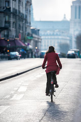 French woman in red coat and beret riding bicycle on Paris street with Notre Dame Cathedral in background