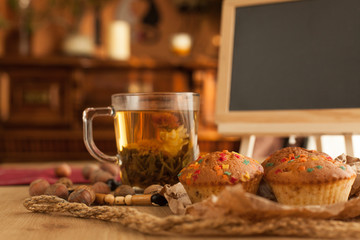 Chinese flower jasmine tea with fresh just baked cupcakes, made with nuts and chocolate set with board to write on it by chalk with sunlight on background.