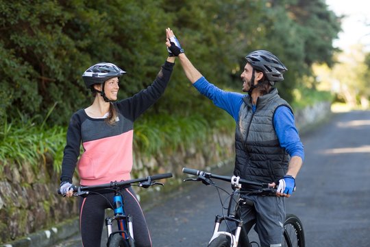 Biker couple giving high five while riding bicycle on the road