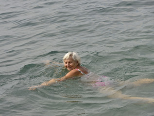 Aged smiling woman is swimming in light clear sea water.