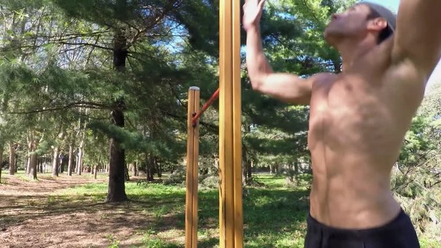Attractive shirtless muscular young man exercising and working out in outdoor gym in city park