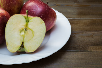 Four fresh red apples in white plate on wooden background