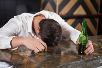 Drunk man lying on a counter with bottle of beer
