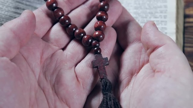 hands holding the Bible and praying with a rosary